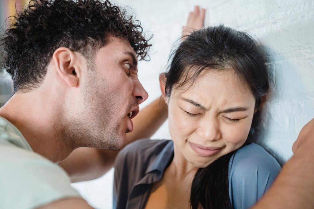 Aggressive man leaning over a woman he has pinned against a wall, while he is yelling at her.